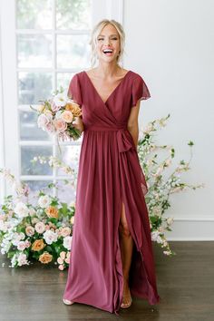 a woman standing in front of a window wearing a red dress and holding a bouquet