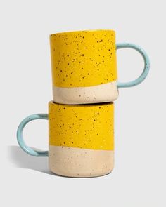 two yellow and white coffee mugs sitting side by side on a gray surface with speckles