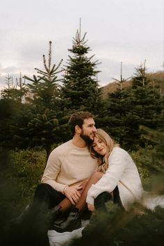 a man and woman sitting next to each other in front of some pine tree trees