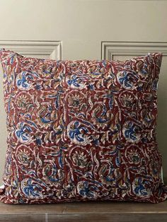 a red and blue pillow sitting on top of a wooden table next to a wall