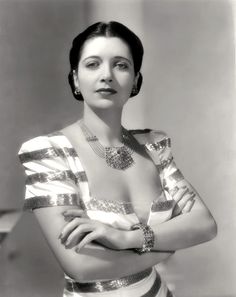 a woman with her arms crossed wearing a white and gold dress, necklace and bracelet