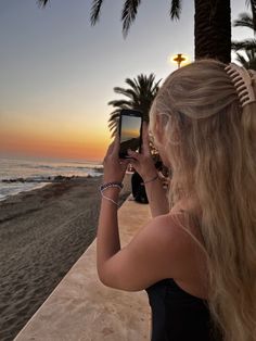 a woman taking a photo on her cell phone at the beach with palm trees in the background