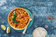 a bowl filled with rice and meat next to a cup of sour cream on a blue table