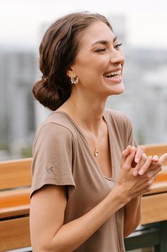 a woman smiling while sitting on a bench with her hands folded in front of her chest