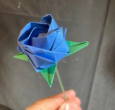 a hand holding a blue origami rose in it's left hand,