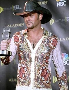 a man wearing a cowboy hat and holding a microphone in his right hand while standing on a red carpet