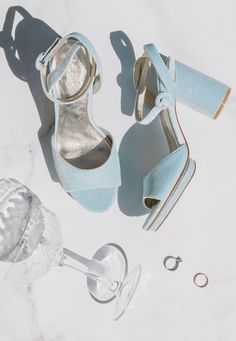 a pair of blue high heeled shoes next to an empty wine glass and other accessories