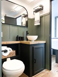 a white toilet sitting next to a sink in a bathroom under a large round mirror