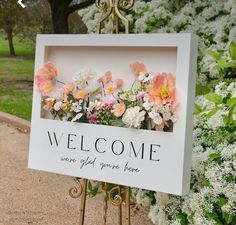 a welcome sign with flowers on it sitting in front of some white and pink flowers