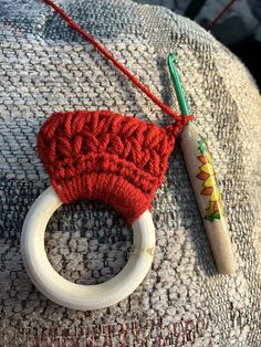 a red knitted object with a wooden ring on it's end next to a crochet hook