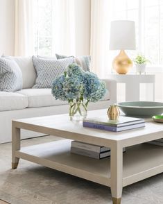 a living room with a white couch, coffee table and blue hydrangeas in the center