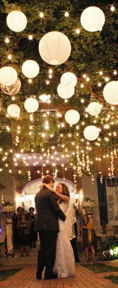 a bride and groom sharing their first dance under lanterns