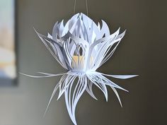 a white paper flower hanging from a string on a gray wall next to a clock