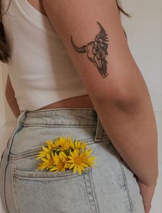 a woman with a cow skull tattoo on her arm and a yellow flower in her pocket