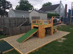 a wooden play set with a slide and sandpit in the back yard, surrounded by grass