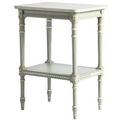 a white end table with an ornate design on the top and bottom shelf, sitting against a white background