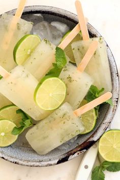 a bowl filled with ice and limes on top of a white counter next to a spoon