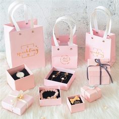 pink gift bags with gold lettering on them and jewelry in small boxes next to each other