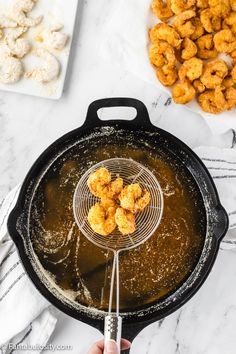 someone is holding a frying pan with tater tots in it and some other food on the table