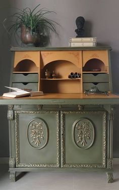 an old fashioned desk with drawers and books on it's top, in front of a potted plant