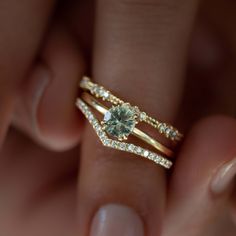 a woman's hand holding a gold ring with a green diamond on top and two diamonds in the middle