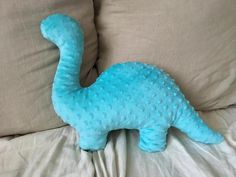 a blue dinosaur stuffed animal laying on top of a bed