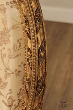 an ornately decorated chair with gold trimmings on the arm and back, in front of a wood floor