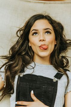 a woman sticking out her tongue while laying on a white couch in front of a pillow