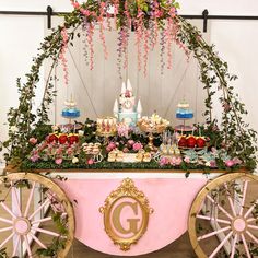 a table topped with lots of cake and desserts next to a pink cart filled with flowers