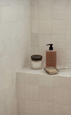 a soap dispenser sitting on top of a shelf in a tiled bathroom