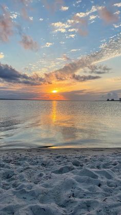 the sun is setting over the ocean with clouds in the sky and sand on the beach