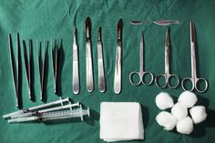 several surgical instruments are laid out on a green tablecloth with cotton swabs