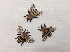 three embroidered bees sitting on top of a white cloth covered in black and yellow thread