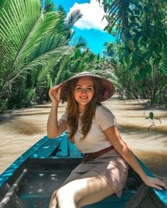 a woman wearing a hat sitting in the back of a blue boat on a river