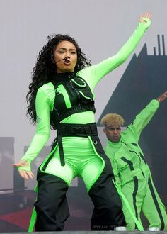 a woman in green and black outfit performing on stage