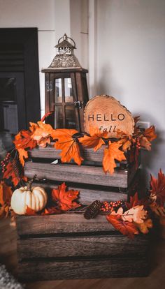 a wooden crate filled with fall leaves next to a lantern and a sign that says hello fall