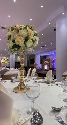 a table with white linens, silverware and flowers in a tall vase on it