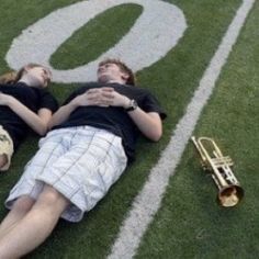 two young men laying on the ground next to a trumpet and trombone horn in front of a football field