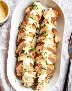 sliced meat covered in sauce and garnished with parsley on a white platter