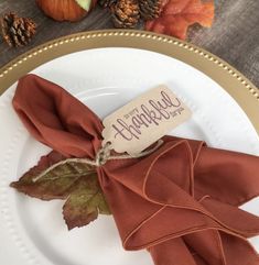 a white plate topped with a napkin and fall leaves next to an empty tag that says happy holidays