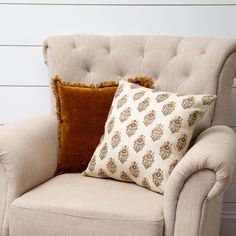 a chair with two pillows on it in front of a white wall and wooden floor