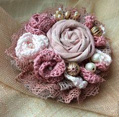 a pink and white flower brooch with pearls in it's center on a piece of fabric