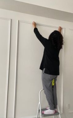 a woman standing on a stepladder painting the wall