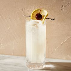 a tall glass filled with ice and a cherry on the rim next to a wall