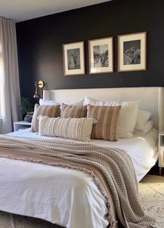 a bedroom with black walls, white bedding and two framed pictures on the wall