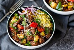 two bowls filled with meat and vegetables on top of a table next to a fork