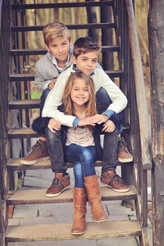 three young children sitting on the steps in front of an old wooden staircase with their arms around each other