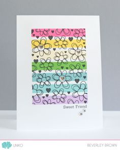 a card with flowers and hearts in different colors, on a white table next to a gray wall