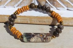 This Unisex Stretch Bracelet is a Fantastic Blend of Smoky Brown Petrified Wood, Smokey Brown/Cream Jasper and Mustard Color Wood Beads.  I used in this unique design - A long cylinder-shaped Ocean Jasper Gemstone in Smoky Brown/Cream with a spot of Blue and Mustard - Unique Smoky Brown Petrified Wood Saucer Beads - Mustard Color Spacer Wood Beads - Bronze Accent Beads. This stretch bracelet should fit up to a size 8-inch wrist.  Let me know if you need a custom size. Earthy Brown Beaded Bracelets With Gemstone Beads, Earthy Brown Jasper Beaded Bracelets, Brown Jasper, Wood Bracelet, Mustard Color, Cylinder Shape, Petrified Wood, Ocean Jasper, Jasper Gemstone