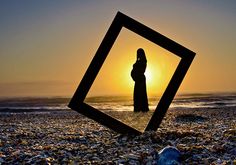 a woman standing on top of a sandy beach next to the ocean at sun set